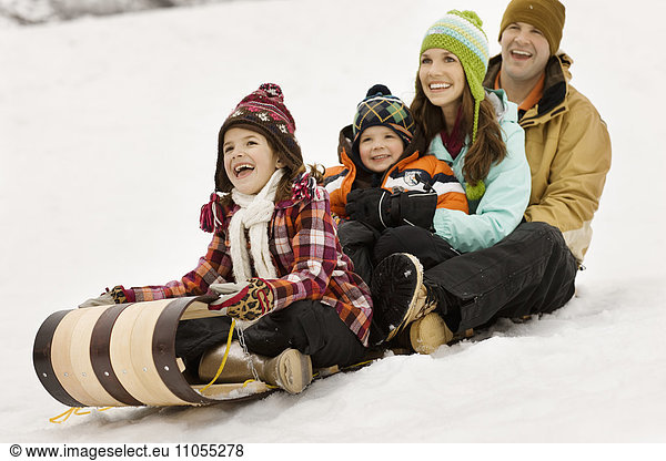 Eine Familie mit zwei Erwachsenen und zwei Kindern sitzt auf Schlitten auf dem Schnee.