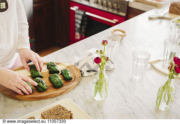 Eine Frau bereitet in einer Küche gefüllte Weinblätter als Mittagsgericht zu.