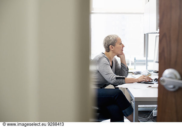 Eine Frau  die allein in einem Büro arbeitet. Sie konzentriert sich auf eine Aufgabe und benutzt einen Computer.