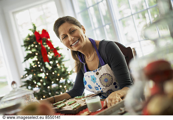 Eine Frau  die an selbstgebackenen Bio-Weihnachtsplätzchen arbeitet und Dekorationen auf grünem Zuckerguss dekoriert und bestreut.