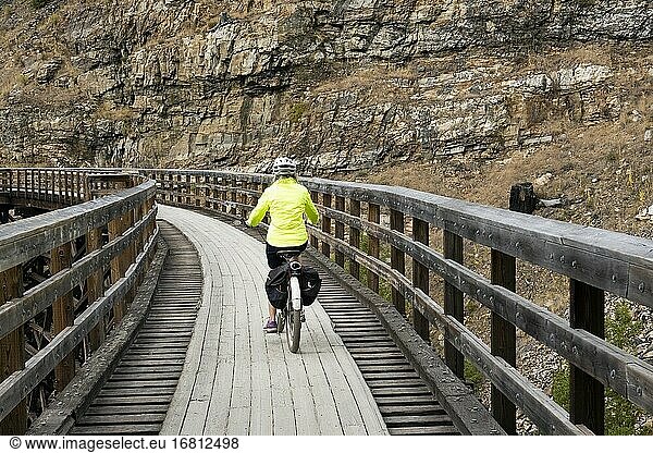 Eine Frau fährt mit dem Fahrrad auf einer Gerüstbrücke im Myra Canyon  auf dem Kettle Valley Rail Trail  Okanagan  British Columbia  Kanada.