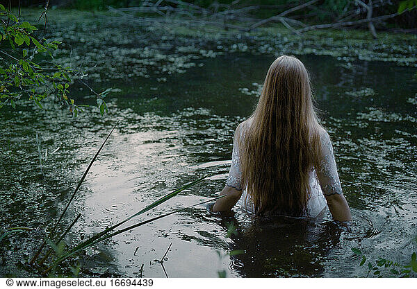 Eine Frau in einem weißen Kleid betritt einen Sumpf.