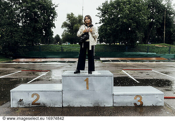 eine Frau in einer weißen Jacke steht im Regen auf dem Podium