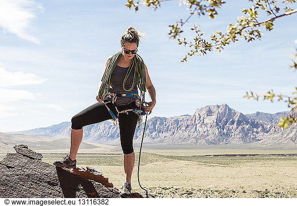 Eine Frau in voller Länge zieht den Sicherheitsgurt an  während sie im Red Rock Canyon National Conservation Area gegen die Berge steht
