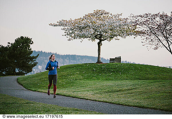 Eine Frau läuft frühmorgens auf einem gepflasterten Weg durch Kirschblüten