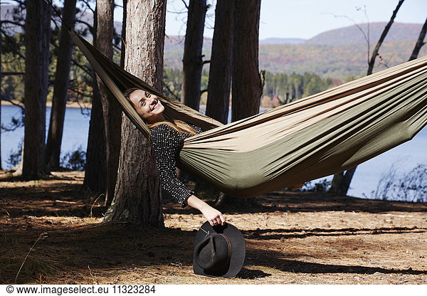 Eine Frau liegt in einer Hängematte und entspannt sich unter den Pinien an einem See.