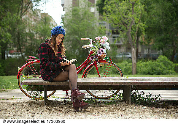 Eine Frau liest ein Buch  ein rotes Fahrrad und ein Korb mit bunten Blumen.