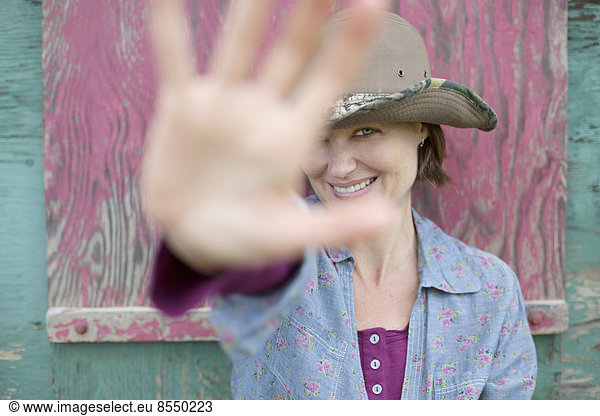 Eine Frau mit einem Hut mit breiter Krempe  die ihre Hand ausstreckt  um die Sicht auf ihr Gesicht zu versperren.