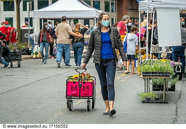 Eine Frau mit Gesichtsmaske zieht ihren Einkaufswagen auf dem Silver Spring Farmers Market  Silver Spring  MD  hinter sich her.