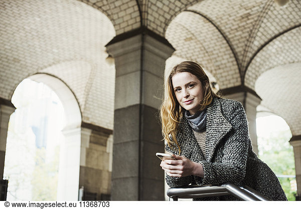 Eine Frau mit langen Haaren  die auf ihr Smartphone schaut  unter einem Torbogen.
