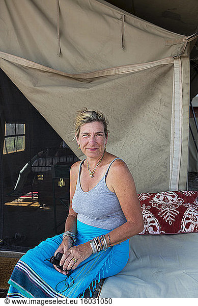 Eine Frau sitzt auf einem Bett in einem Zelt in einem Wildreservatscamp.