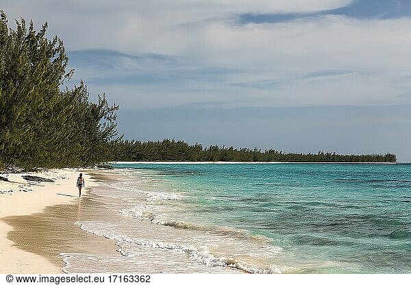 Eine Frau spaziert entlang der Küste mit Wellen und türkisfarbenem Wasser in der Nähe des Orange Creek auf Cat Island  Bahamas.