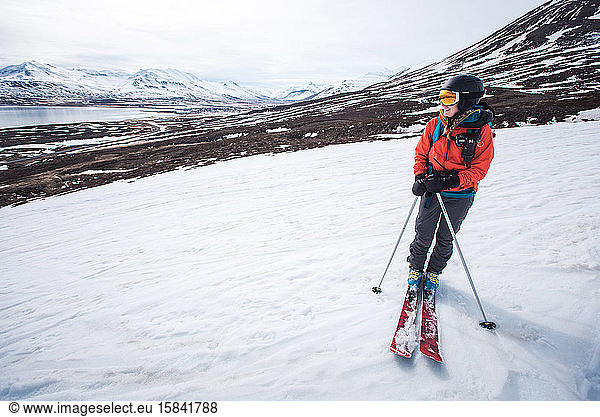 Eine Frau steht mit Skiern auf Schnee mit Bergen und Wasser dahinter