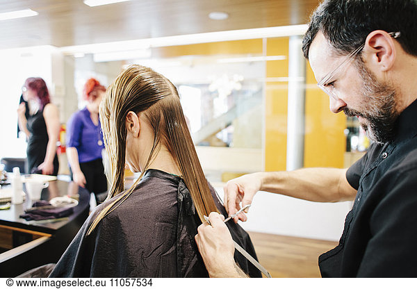 Eine Friseurin mit einer Kundin  die ihr langes  glattes Haar schneidet.