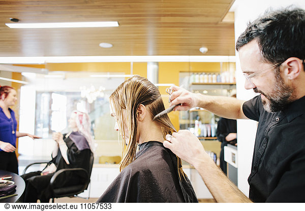 Eine Friseurin mit einer Kundin  die ihr langes Haar abschnittsweise kämmt.