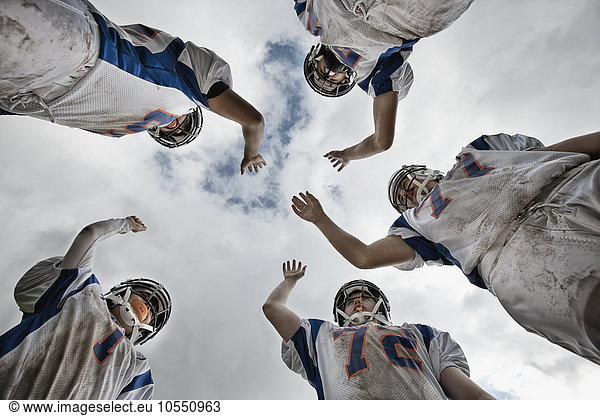 Eine Gruppe von Fussballspielern  Jugendliche in Sportuniform und mit Schutzhelmen  in einem Team  das sich von unten betrachtet zusammenrollt.