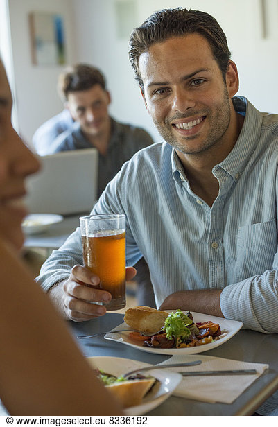 Eine Gruppe von Männern und Frauen in einem Café  die essen und trinken und die Gesellschaft des anderen genießen.