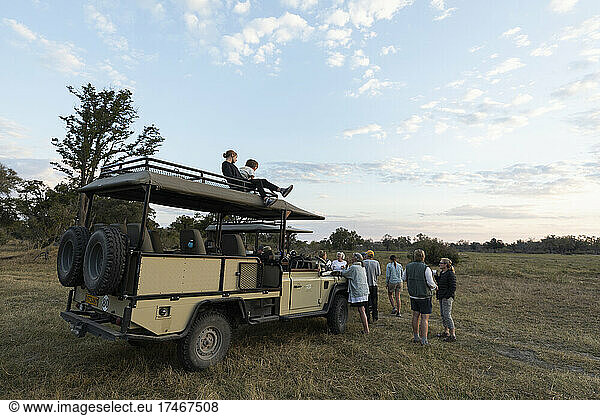 Eine Gruppe von Menschen  die bei einer frühmorgendlichen Pirschfahrt um ein Safari-Fahrzeug herumstehen