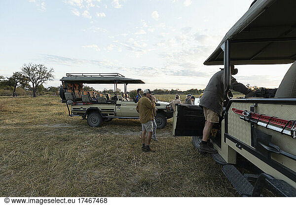 Eine Gruppe von Menschen  die bei einer frühmorgendlichen Pirschfahrt um ein Safari-Fahrzeug herumsteht
