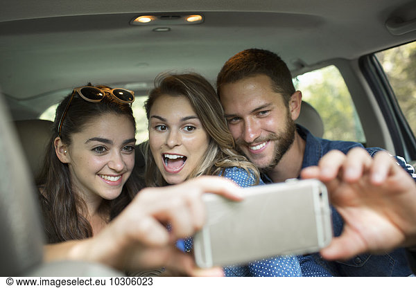 Eine Gruppe von Menschen in einem Auto  zwei Frauen und ein Mann  die ein Selfy nehmen.