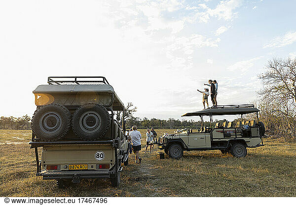 Eine Gruppe von Menschen steht bei einer frühmorgendlichen Pirschfahrt um ein Safari-Fahrzeug herum