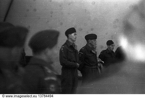 Eine Gruppe von Soldaten steht in formeller Uniform und mit Kopfbedeckung auf. Ein Mann hat eine Brille auf.