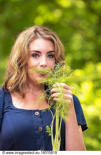 Eine hübsche 37-jährige rothaarige Frau in einem Garten  die an einem Fenchelkraut riecht.