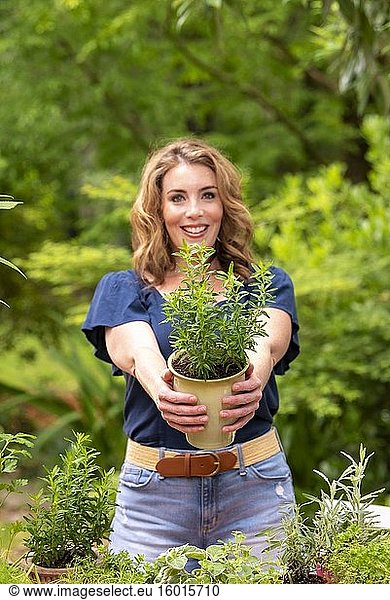 Eine hübsche 37-jährige rothaarige Frau in einem Garten  die eine kleine Bohnenkrautpflanze im Topf hält.