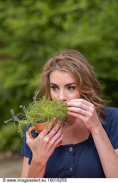 Eine hübsche 37-jährige rothaarige Frau in einem Garten  die eine kleine getopfte Kamillenpflanze hält.