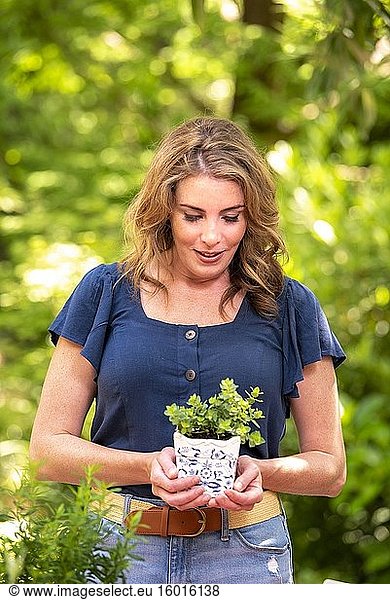 Eine hübsche 37-jährige rothaarige Frau in einem Garten  die eine kleine Oregano-Topfpflanze hält.
