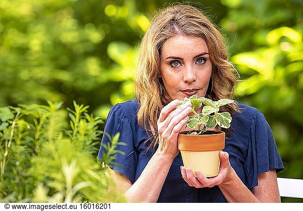 Eine hübsche 37-jährige rothaarige Frau in einem Garten  die eine kleine Plectranthus-Topfpflanze hält.