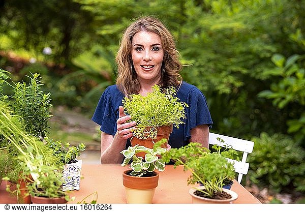 Eine hübsche 37-jährige rothaarige Frau in einem Garten mit einer Buchsbaum-Basilikumpflanze.