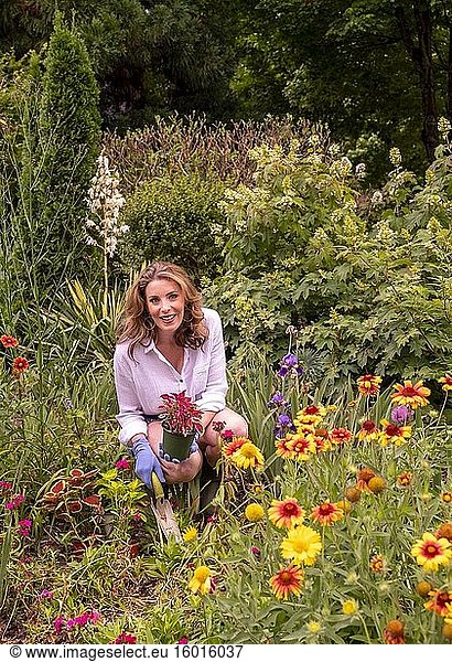 Eine hübsche 37-jährige rothaarige Frau in einem Garten  umgeben von ein- und mehrjährigen Pflanzen im Frühsommer.