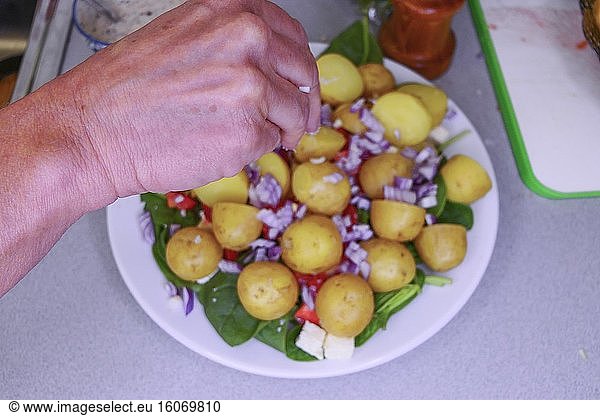 Eine Hand streut Salz auf eine frisch gekochte Kartoffel auf einem Teller mit Spinat  Zwiebeln und Käse.