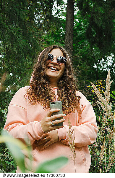Eine junge Frau in einem rosa Sweatshirt  mit Sonnenbrille  mit einem Telefon  lacht