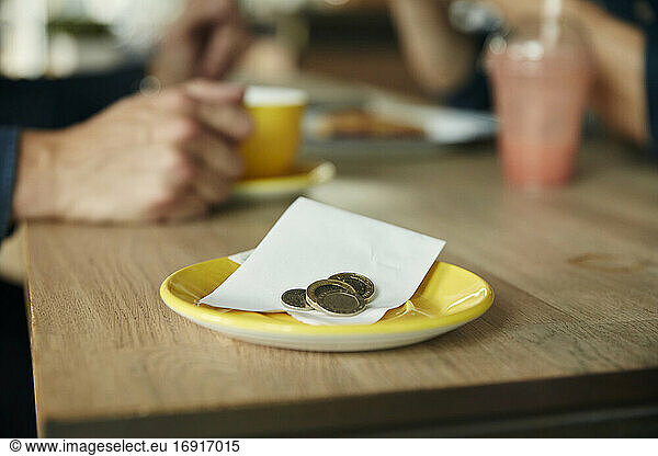 Eine kleine Untertasse mit einem Kassenbon und Münzen  Bargeld auf einem Cafétisch.