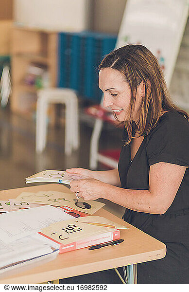 Eine lächelnde Lehrerin ordnet ihre Alphabet-Bildkarten auf ihrem Schreibtisch.