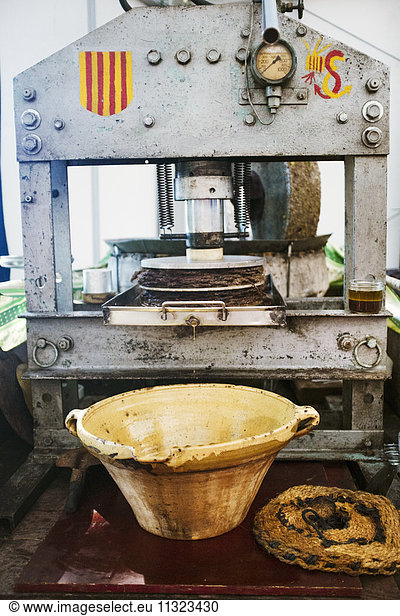 Eine Olivenpresse  eine mechanische Zerkleinerungsmaschine mit Presse und ein kleiner Strom von Olivenöl  der in eine Schüssel fließt.