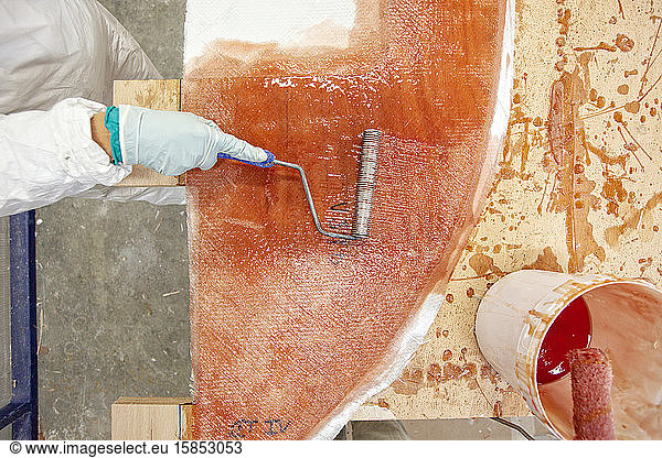 eine Person  die Fiberglas auf eine Form in einer Bootsbaufabrik aufbringt