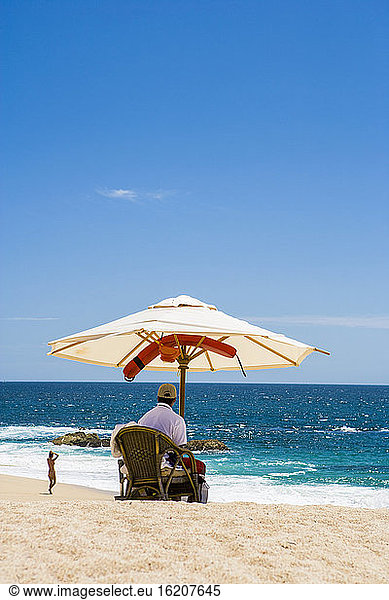 Eine Person  die unter einem Sonnenschirm an einem weißen Sandstrand am Meer sitzt