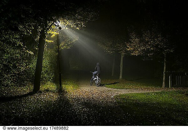 Eine Person fährt an einem dunklen und kalten Herbstmorgen mit dem Fahrrad durch eine einsame Parkanlage in Markt Schwaben  Bayern  Deutschland  Europa