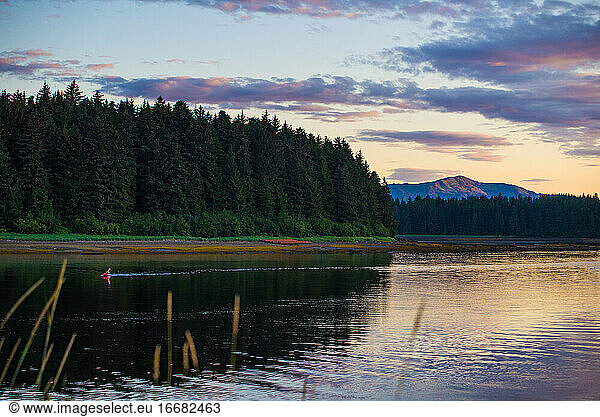Eine Person in einem Packraft paddelt bei Sonnenuntergang durch eine Bucht in Alaska