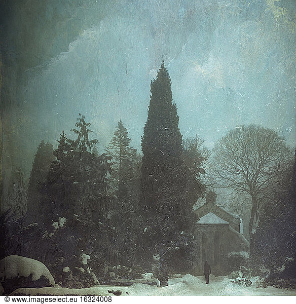 Eine Person steht vor einer verschneiten Friedhofskapelle