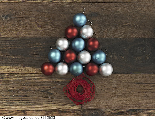 Eine Sammlung blauer  roter und silberner Ornamente  die in Dreiecksform auf einem Holzbrett angeordnet sind. Eine Weihnachtsbaumform mit einem roten Band  das an der Basis aufgewickelt ist.