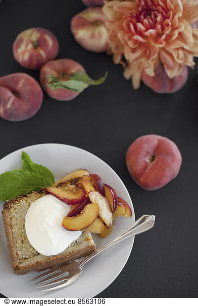 Eine Tabelle von oben betrachtet. Bio-Obst  Pfirsiche und Blumen. Ein Teller mit frischem Obst  Kuchen und Crème fraîche. Eine Gabel. Ein Dessert.