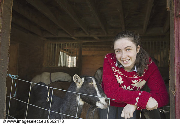 Eine Ziegenfarm. Ein junges Mädchen  das sich an die Absperrung des Ziegenstalls lehnt  mit einer Gruppe von Ziegen hinter ihr.