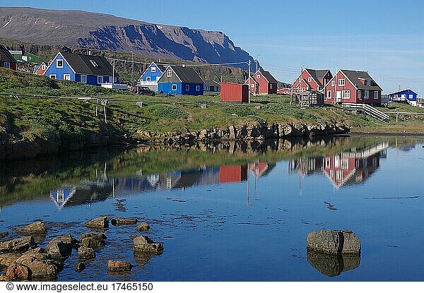 Einfache Holzhäuser spiegeln sich in einem Gewässer  rotes Gestein  ruhige Abendstimmung  Disko Insel  Qeqertarsuaq  Disko Bucht  Nordamerika  Grönland  dänemark  Nordamerika