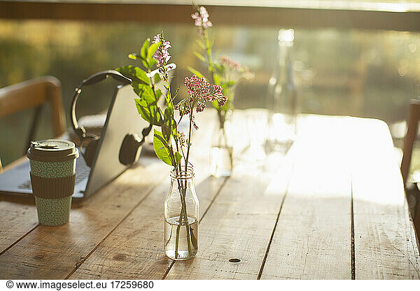 Einfaches Wildblumenarrangement in Glasflasche auf rustikalem Cafétisch