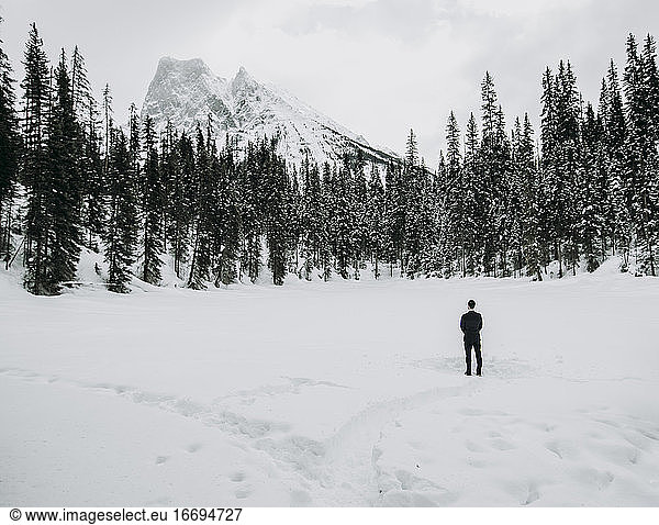 einsamer Mann im Anzug steht allein auf einem schneebedeckten See mit Bergen