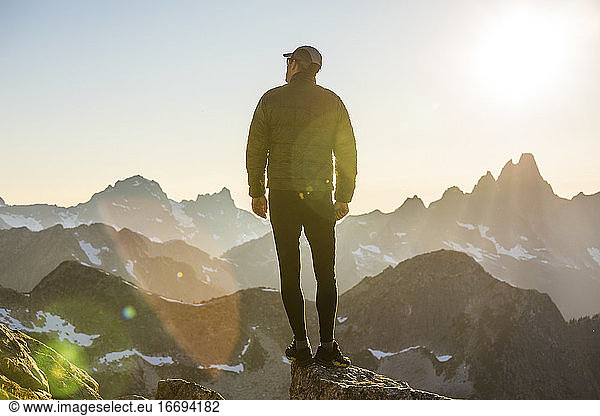 Einsamer Wanderer auf Berggipfel bei Sonnenuntergang mit Aussicht.